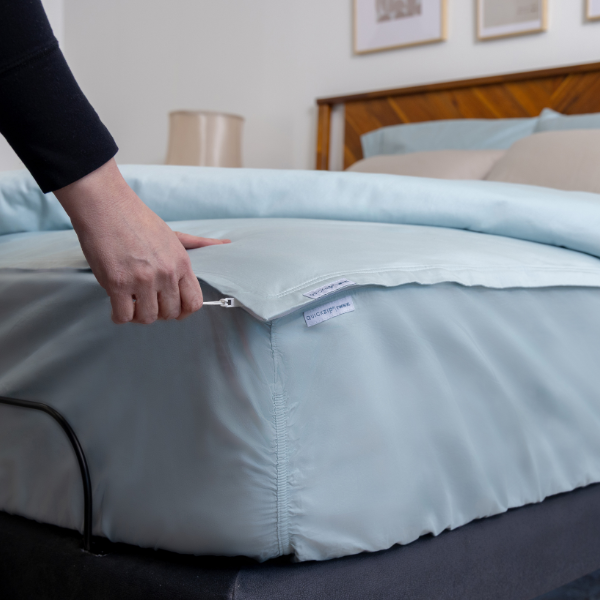 A woman zips a blue fitted sheet onto her mattress