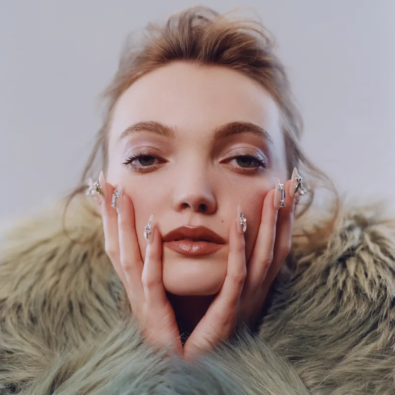 Model wearing green fuzzy coat and bold nail art