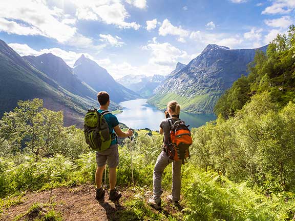 2 Wanderer schauen auf einen Bergsee, umgeben von riesigen Bergen.