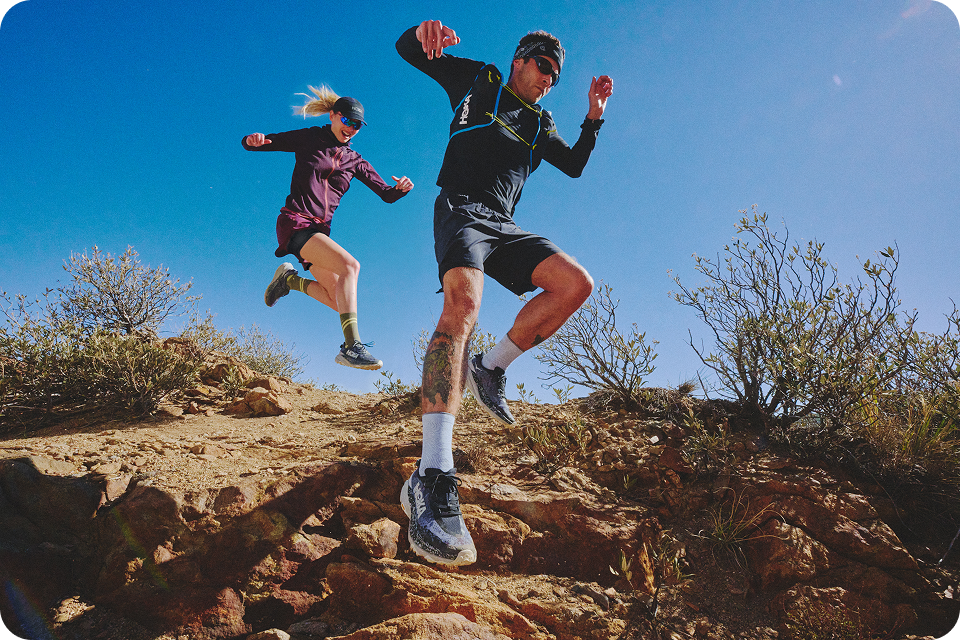Two people running on the trails wearing Speedgoat 6.
