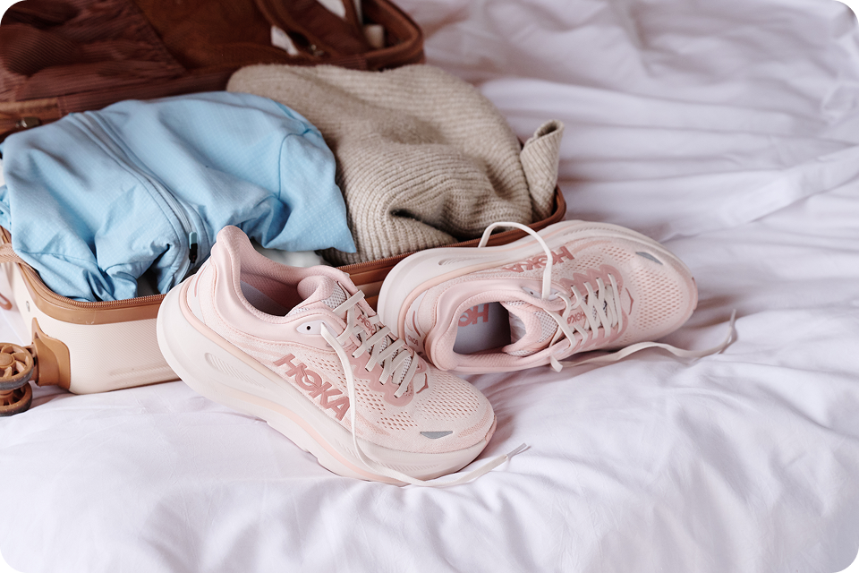An open and unpacked luggage on a bed, with a pair the Bondi 10 in rose latte / rose cream.