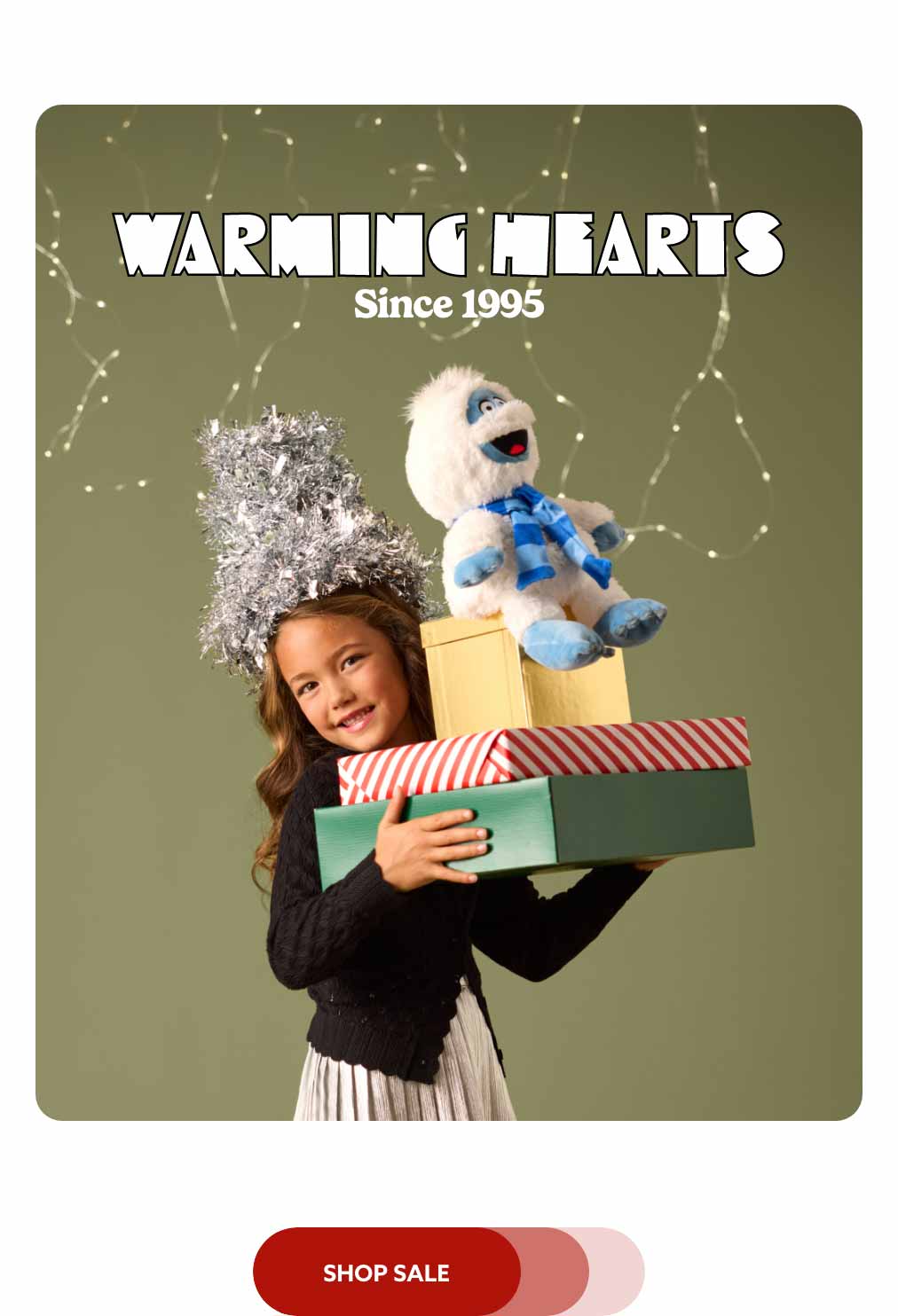 A little girl holding a stack of gift boxes with Bumble Warmies balanced on top. Shop Sale