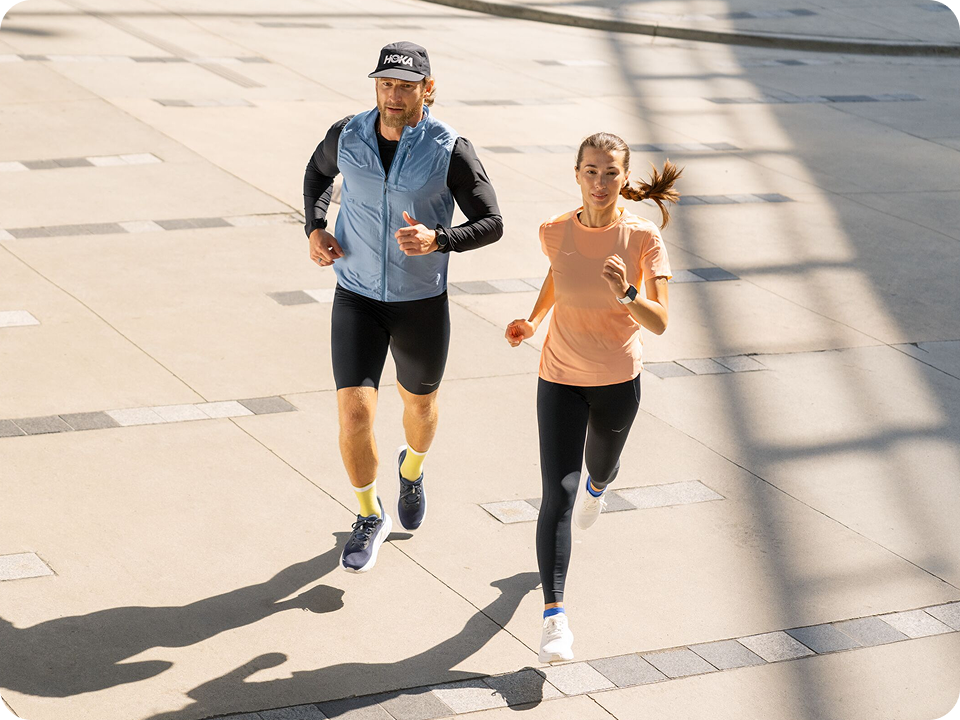 An image of two people running with on concrete ground with their shadows cast to the left of them.