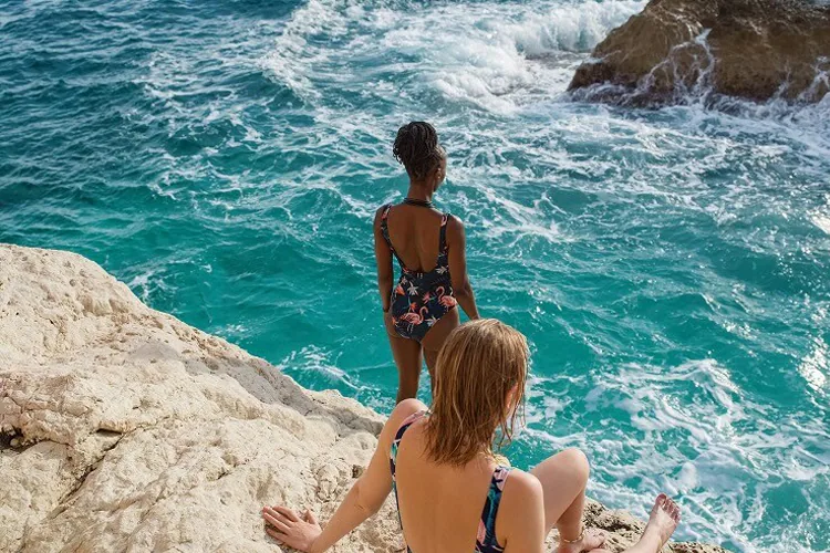 Two women on a rock look out over green-blue waters