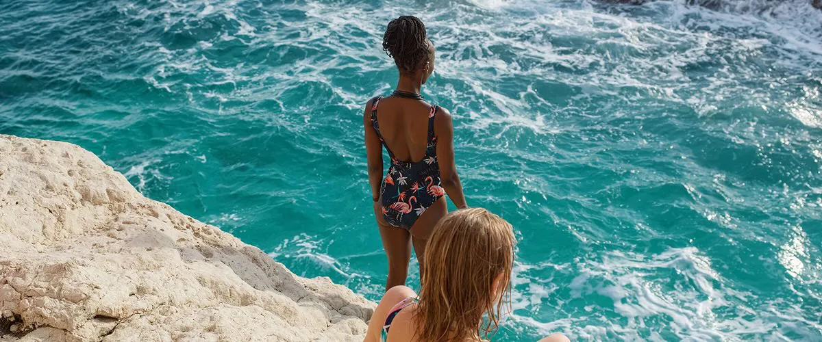Two women on a rock look out over green-blue waters