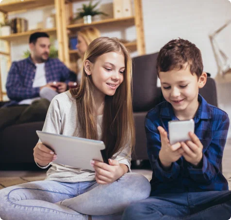 Two young children are smiling and holding digital devices.