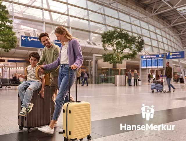 A family strolls carefree through the airport building with their suitcases. Book travel insurance now.