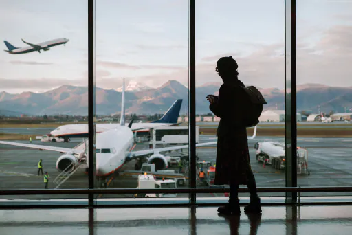 A traveller stands in an airport terminal watching a plane take off.