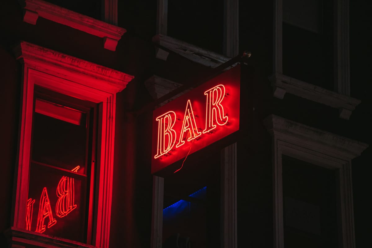 A neon "Bar" sign lights up the neighborhood at night.