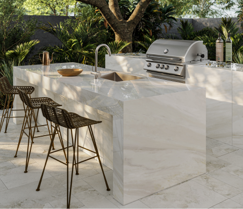 Outdoor kitchen with a built-in grill, sink, and bar. The countertops and flooring are large format marble-look tile.