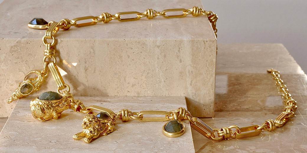 A gold-plated necklace with animal-shaped pendants arranged on a marble block. – Shop New In.