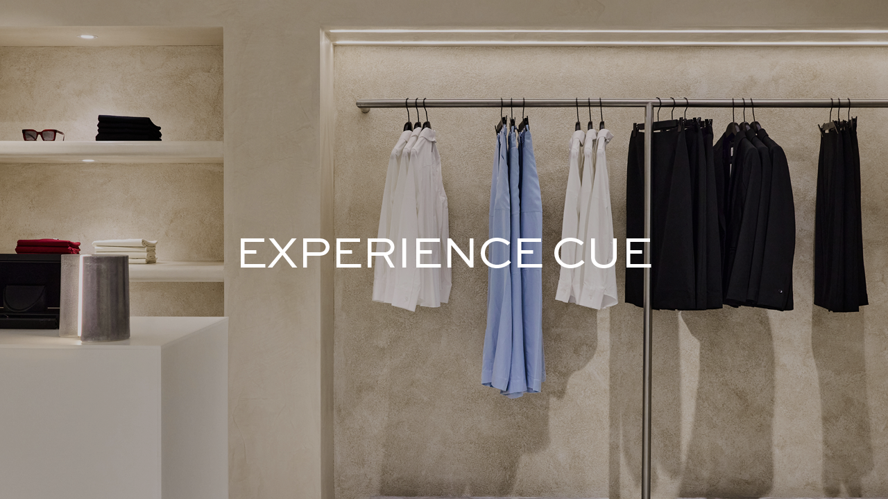 Minimalist retail display with white and blue shirts, black suits on hangers, and text 'EXPERIENCE CUE' overlaid.