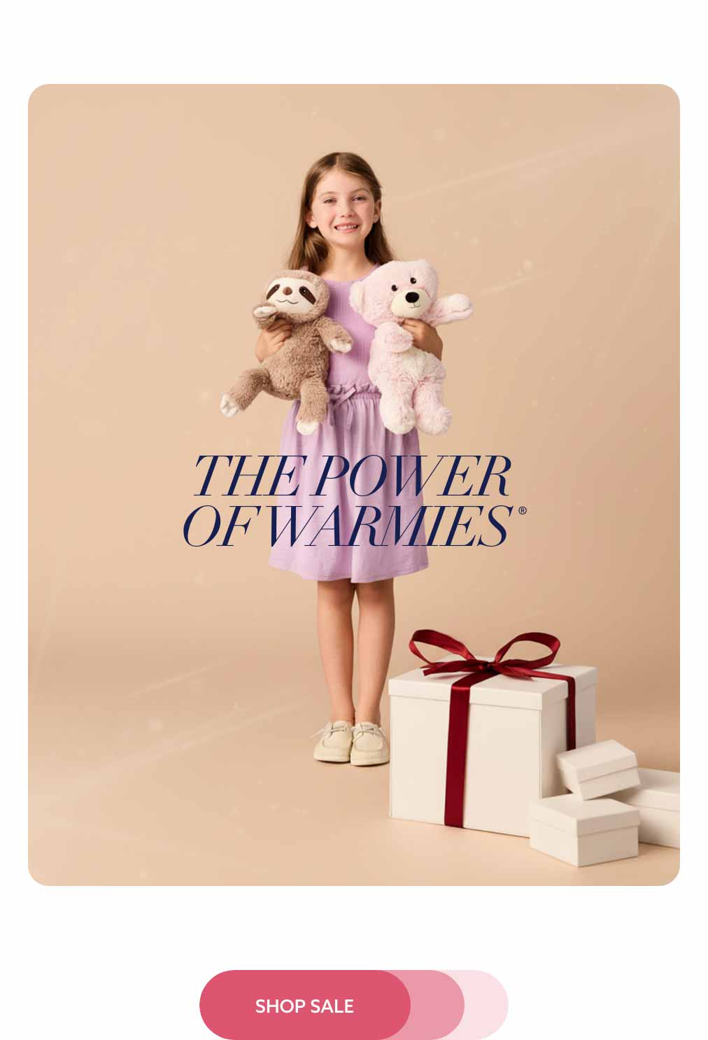 A little girl holding Sloth and Marshmallow Bear Warmies with gift boxes around her. Shop Sale.