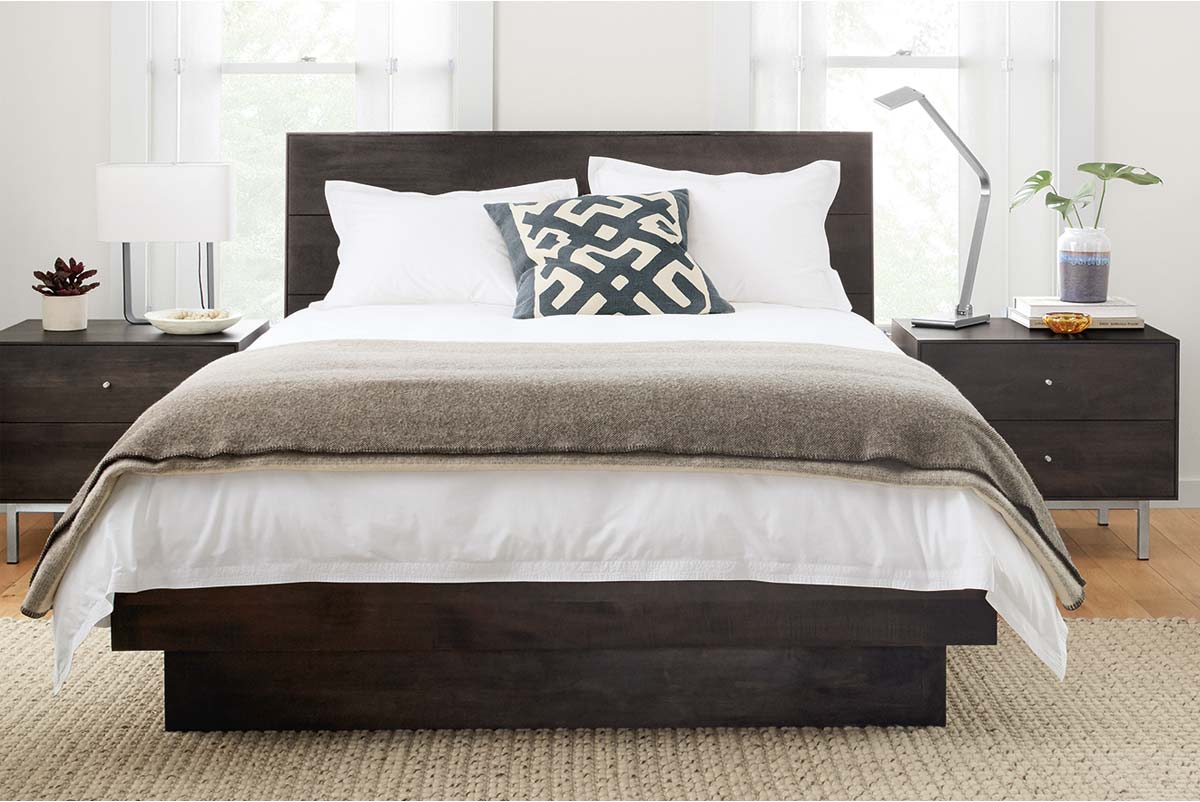 Dark wood Hudson bed in styled with grey throw and geometric pillow between matching nightstands and lamps.