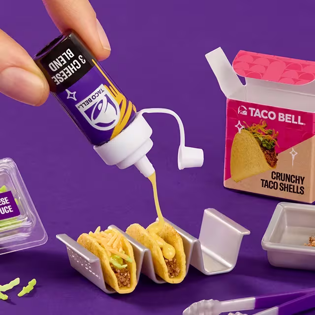 Hand squeezing mini Nacho Cheese Sauce onto a mini Taco from Miniverse.