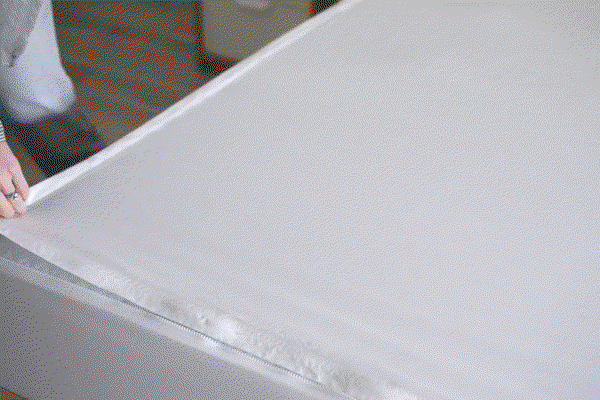 A woman zips a new fitted sheet onto her bed