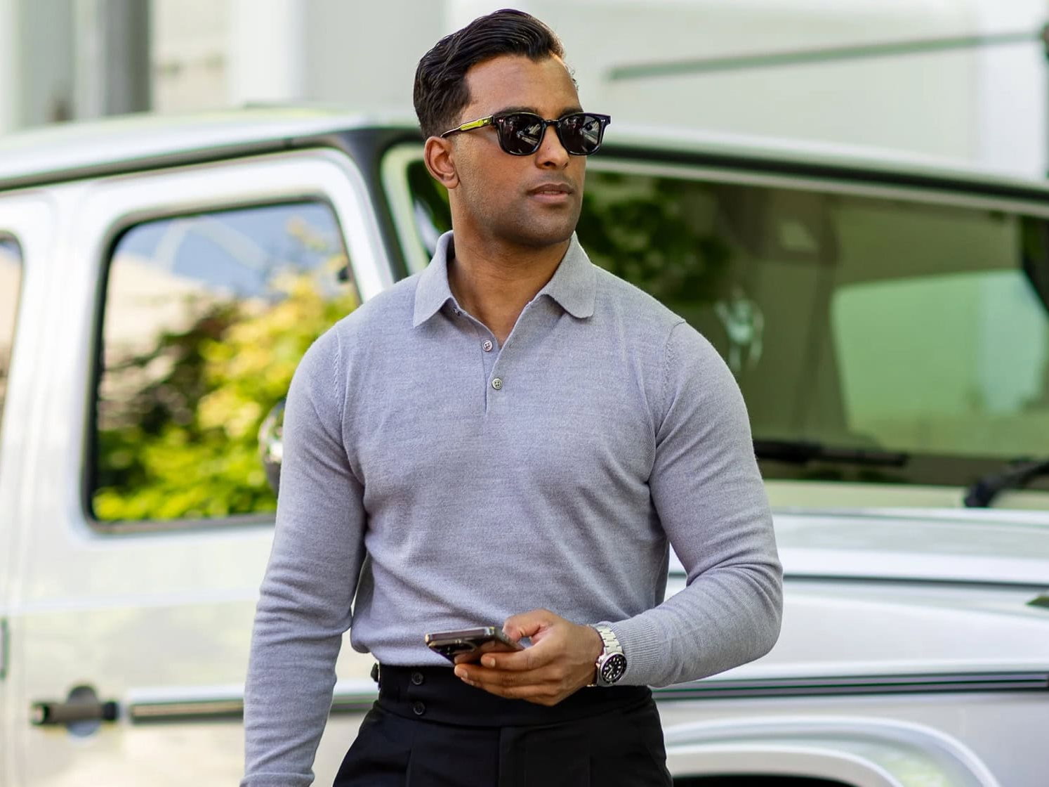 a man wearing a gray shirt and sunglasses holding a cell phone