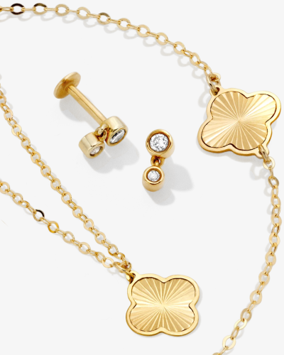 Gold clover-shaped pendant necklaces paired with small diamond-accent stud earrings.