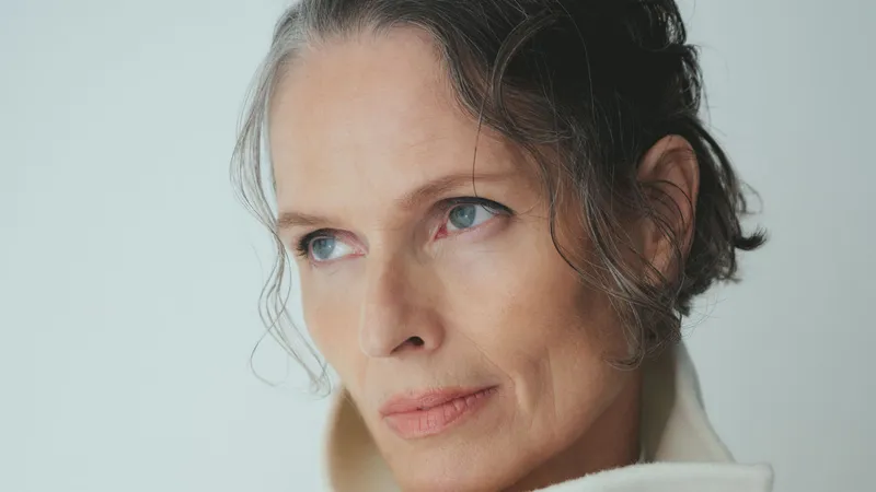 Image contain a model in a white turtleneck sweater on a gray background