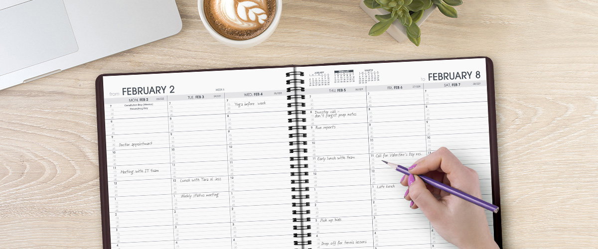 A woman’s hand at a desk writing in an AT-A-GLANCE appointment book