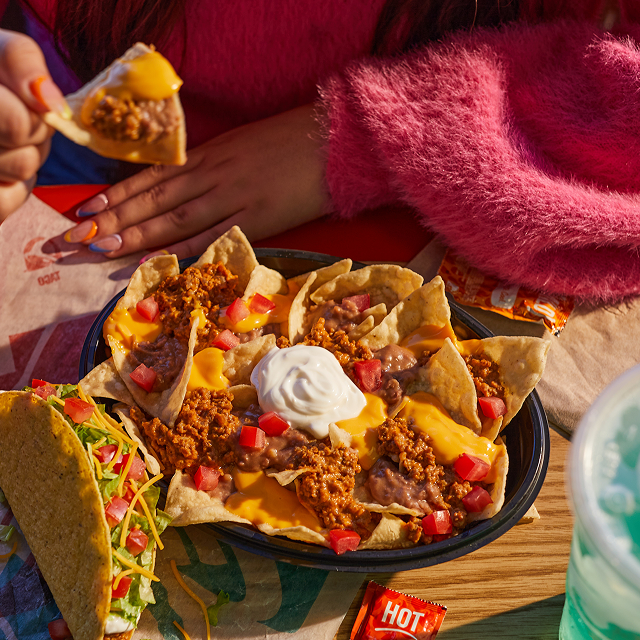 A person in a fuzzy read coat sitting at a table enjoying a Nachos Bell Grande®.