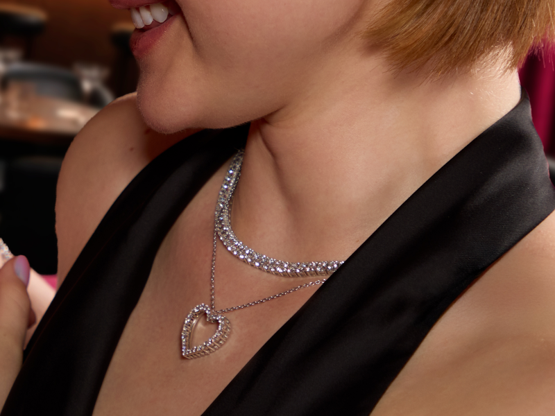 Female model smiling and wearing a layered diamond necklace with a heart pendant.