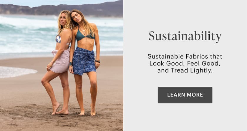 Women standing together on beach wearing swim tops and sarongs. 