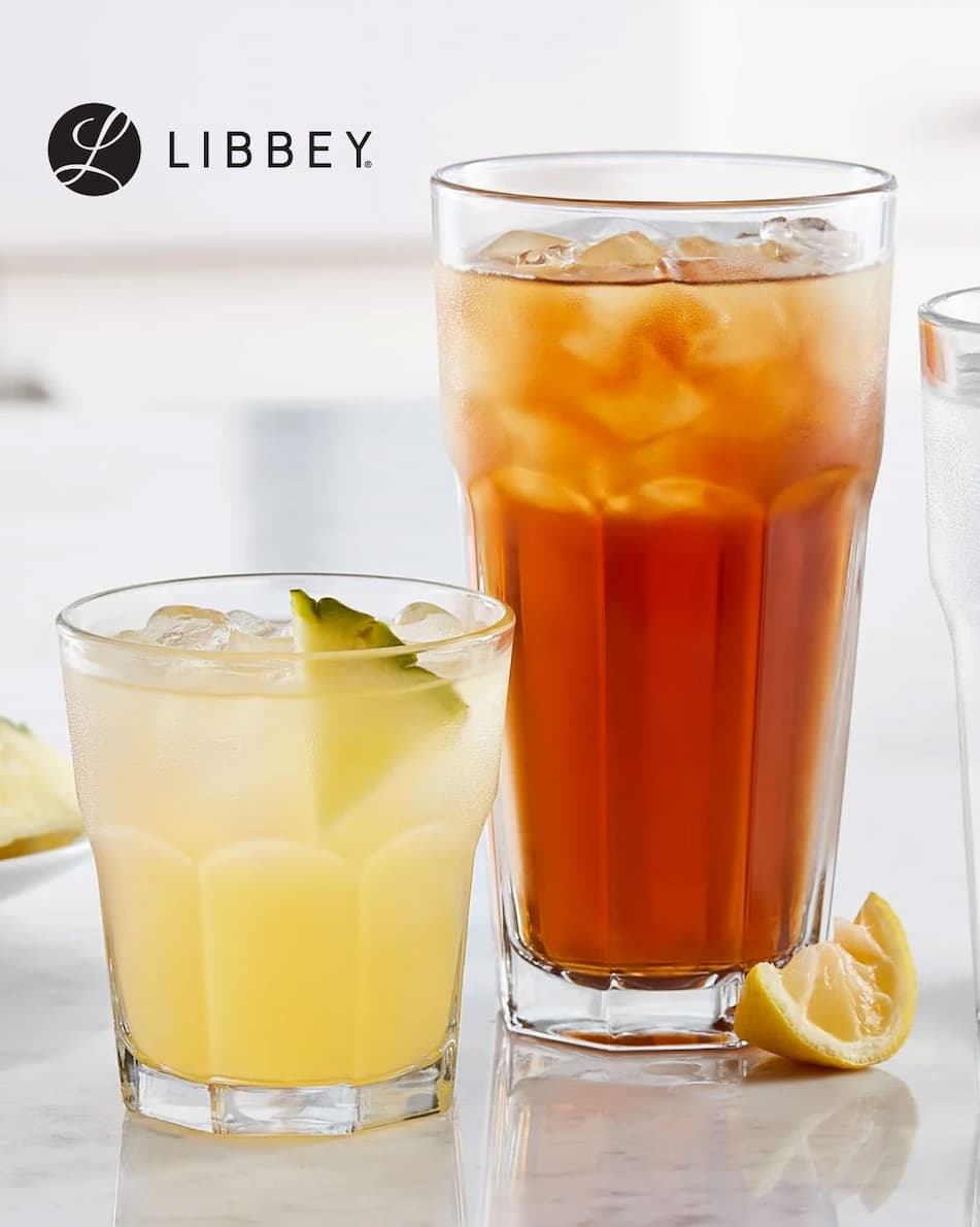A short Gibraltar Rocks Glass filled with an ice cold drink and pineapple wedge next to a tall Gibraltar Tumbler Glass filled with iced tea and a lemon wedge beside it.