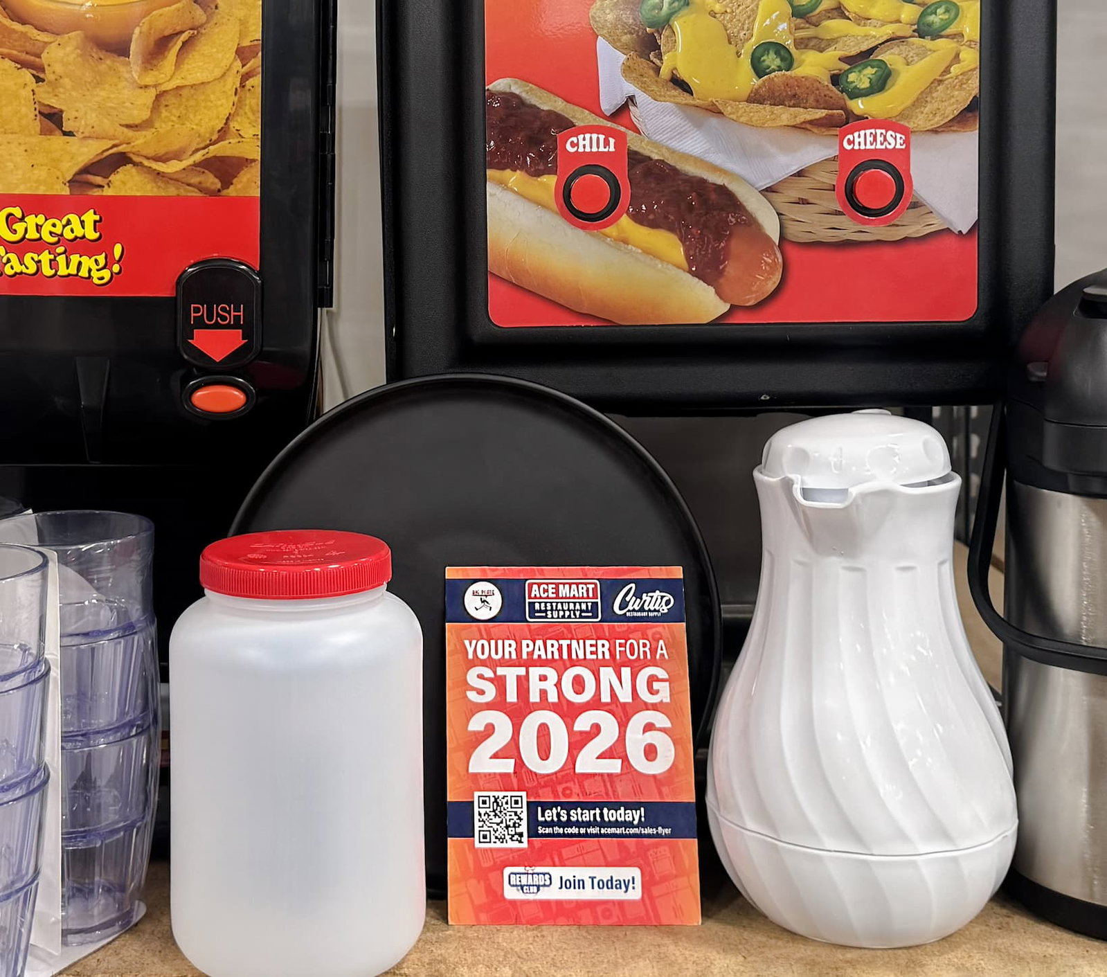 A nacho cheese machine from Gold Medal, Chef's Supreme tumblers, a bar backup with red lid, and Chef's Supreme Insulated Carafe pictured by the Ace Mart sales flyer printed material.