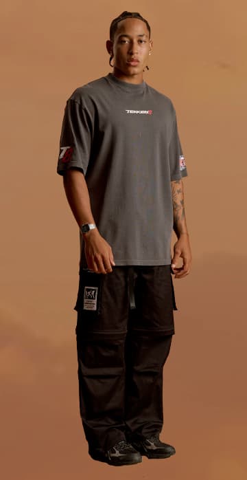 an image of a man standing in a desert wearing a grey shirt and black cargo pants