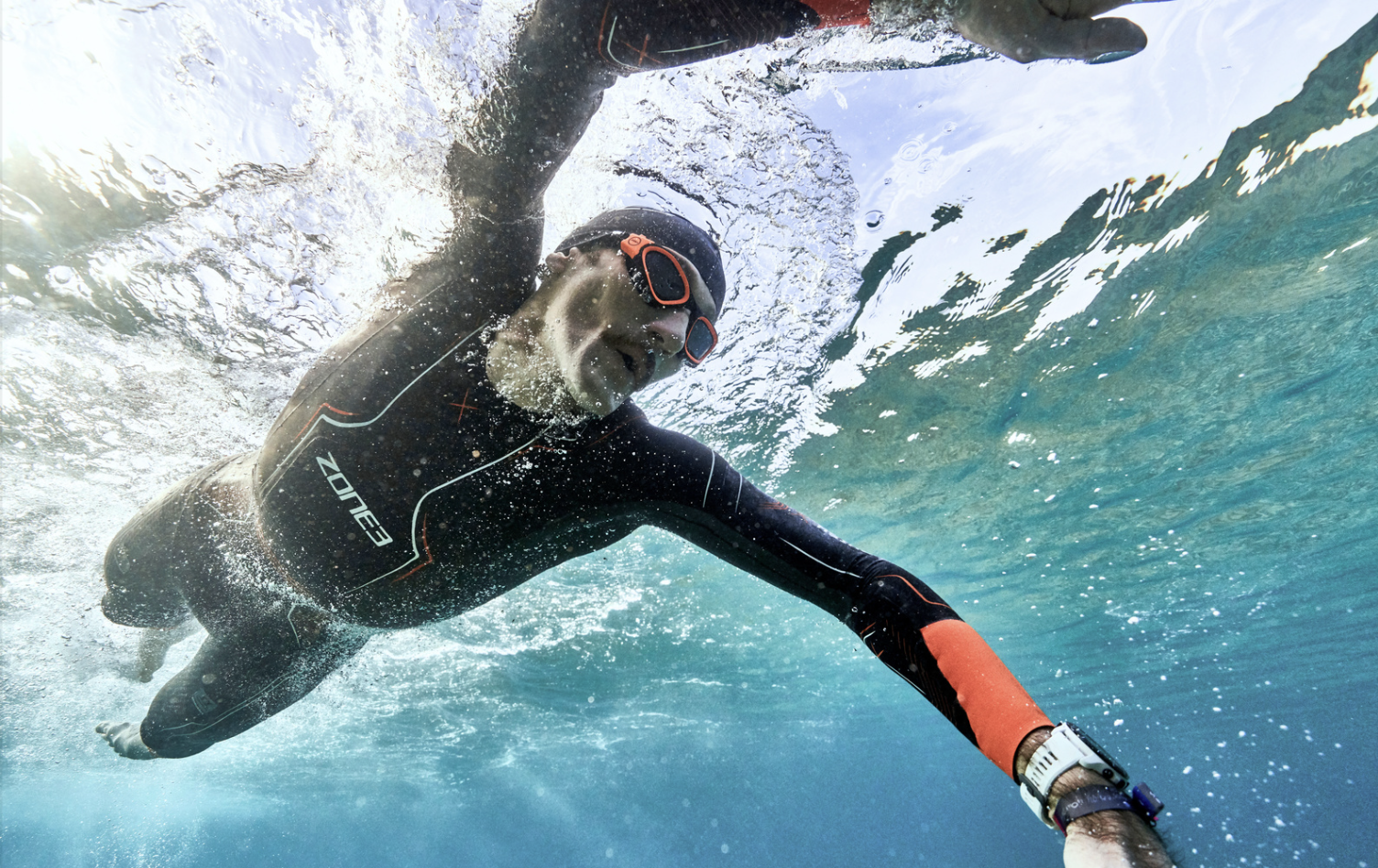 The Science Behind Zone3. | The image shows and athlete swimming, wearing a ZONE3 wetsuit, branded silicone cap and goggles.