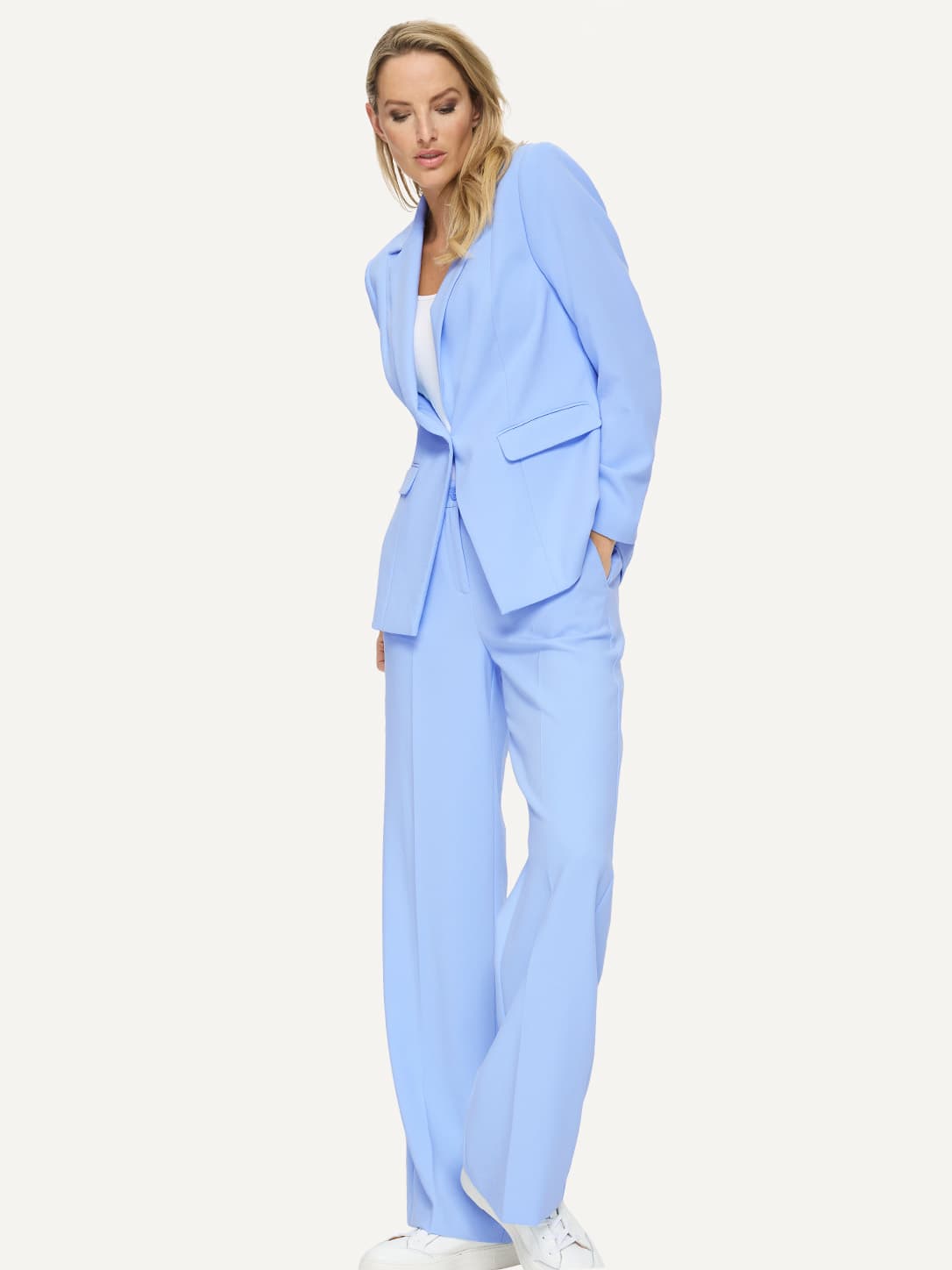 Een model draagt een lichtblauwe blazer met bijpassende wijde broek en wit topje, gecombineerd met witte schoenen. 