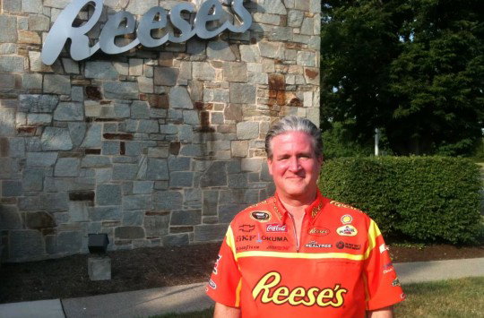 Brad Reese wearing an orange Reese's shirt in front of a Reese's logo on an exterior wall