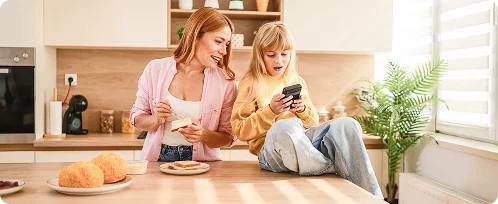 Photo of a mother and daughter in a kitchen looking at a cell phone.