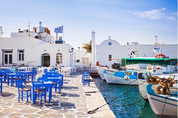 A vibrant Greek harbor with white buildings, blue tables, and fishing boats.