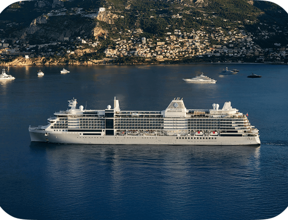 A Silversea cruise ship sails past a Mediterranean coastline with yachts.