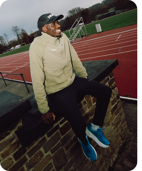 An image of a person posing on a track pointing towards the HOKA logo on their jacket, and an image of a person sitting on a brick wall smiling by a track.