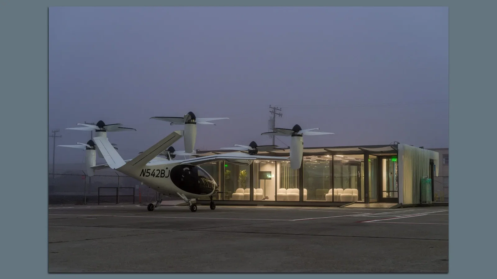 White Joby electric air taxi, with four rotors ,sits on the tarmac at dusk beside a glass-walled lounge known as a vertiport; interior chairs glow, 