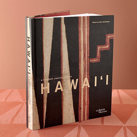 Hardback exhibition book standing on a patterned kapa-inspired surface with a brown background. - Shop the Book.