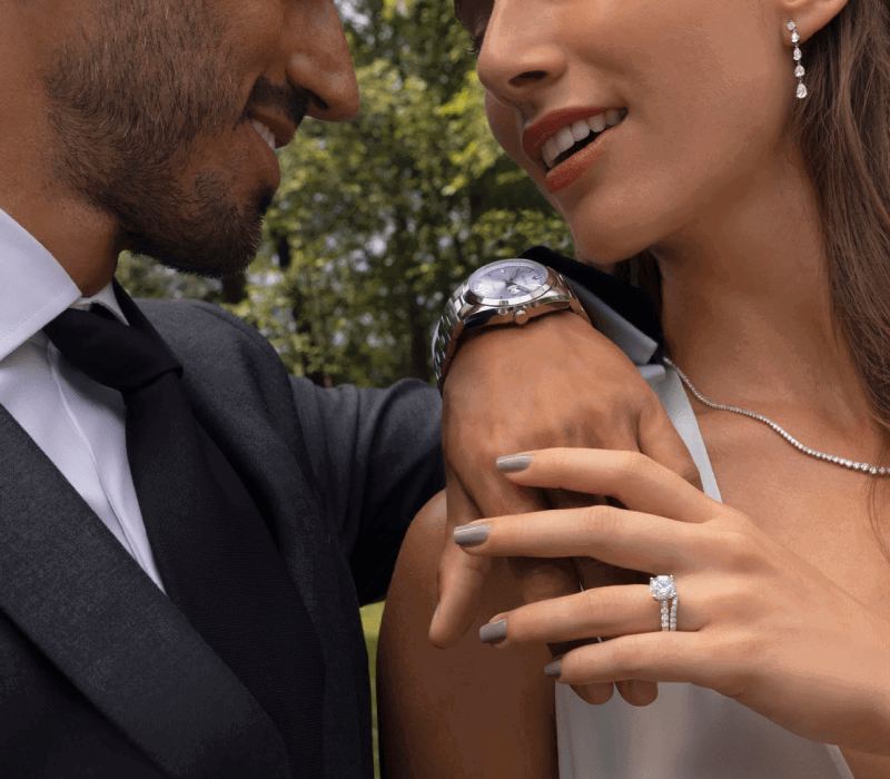Newlywed couple. Man wearing silver watch. Woman wearing variety diamond jewelry.