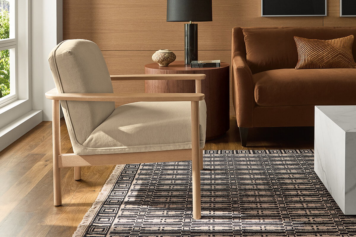 Renew lounge chair with a cream cushion next to a brown leather sofa, with a round side table, lamp, and patterned rug.