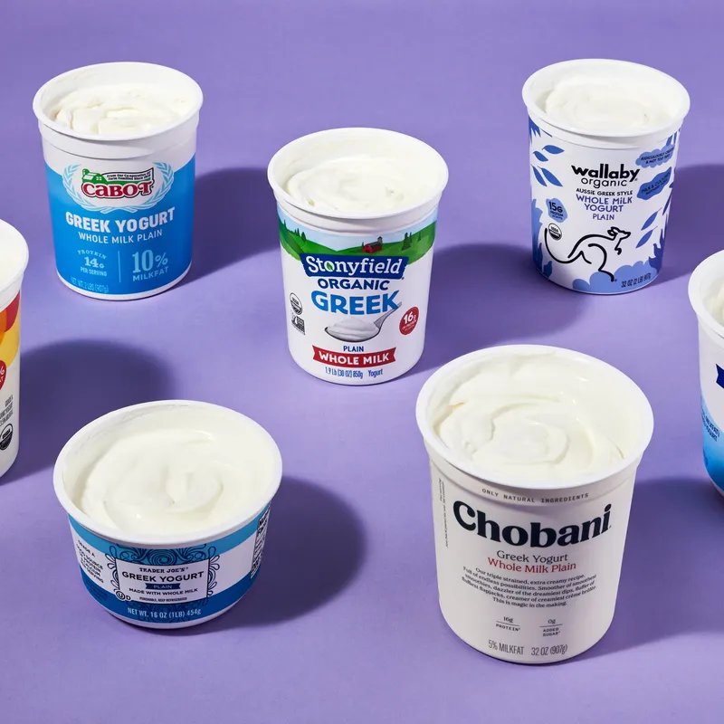 Seven containers of open greek yogurt on purple background.