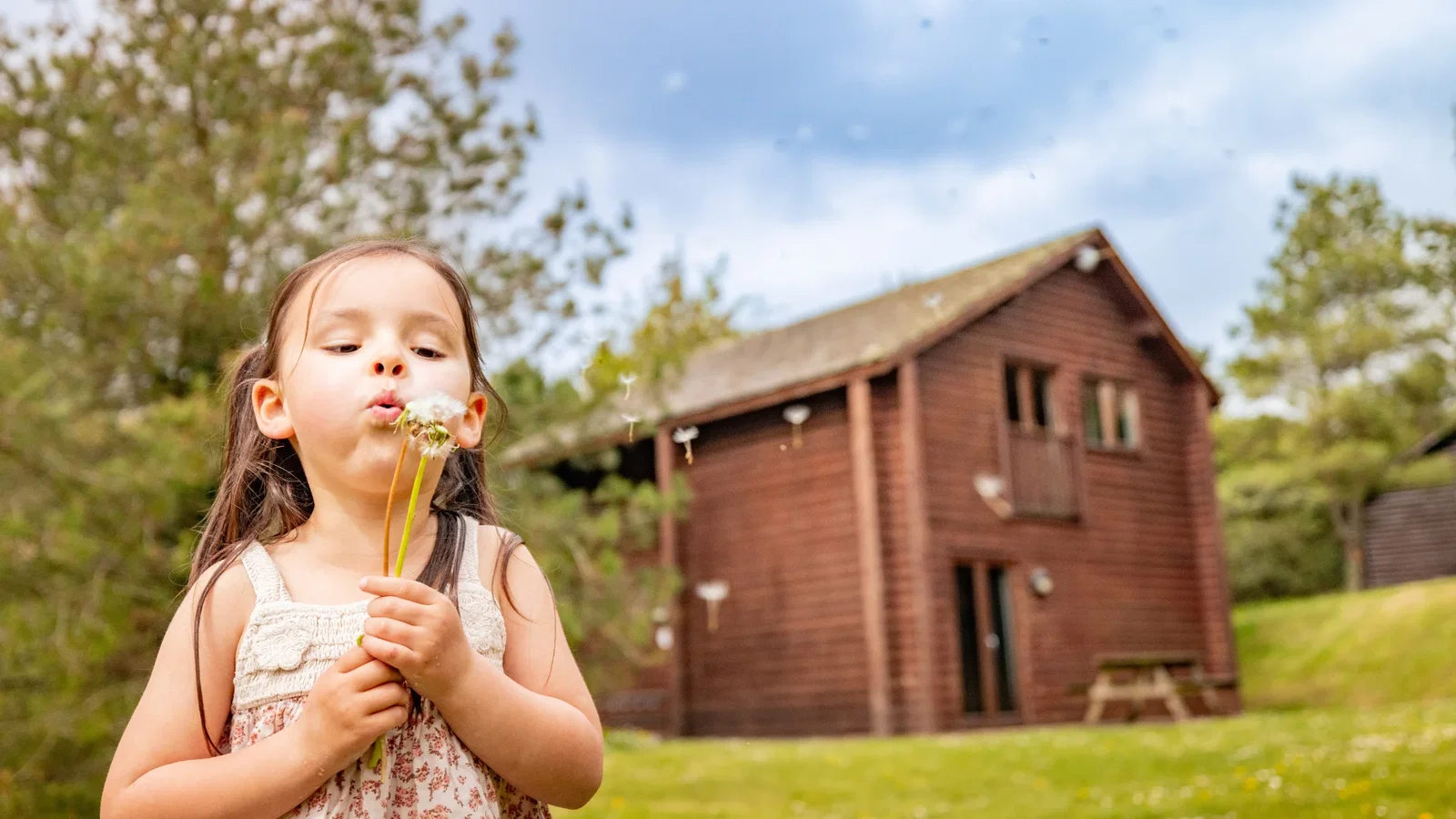 girl blowing dandelion infront of lodge at spring