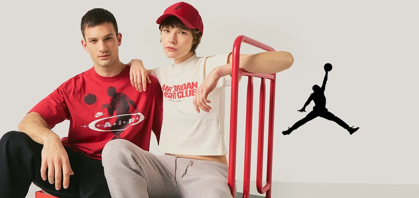 Twee jonge volwassenen zitten op een rode vlakke kar; de ene draagt een rood T-shirt met afbeelding, de andere een wit cropped T-shirt en een rode pet.