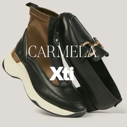 Mocasín de cuero negro con hebilla de oro junto a zapatilla negra y marrón con cremallera y suela blanca sobre fondo neutro.