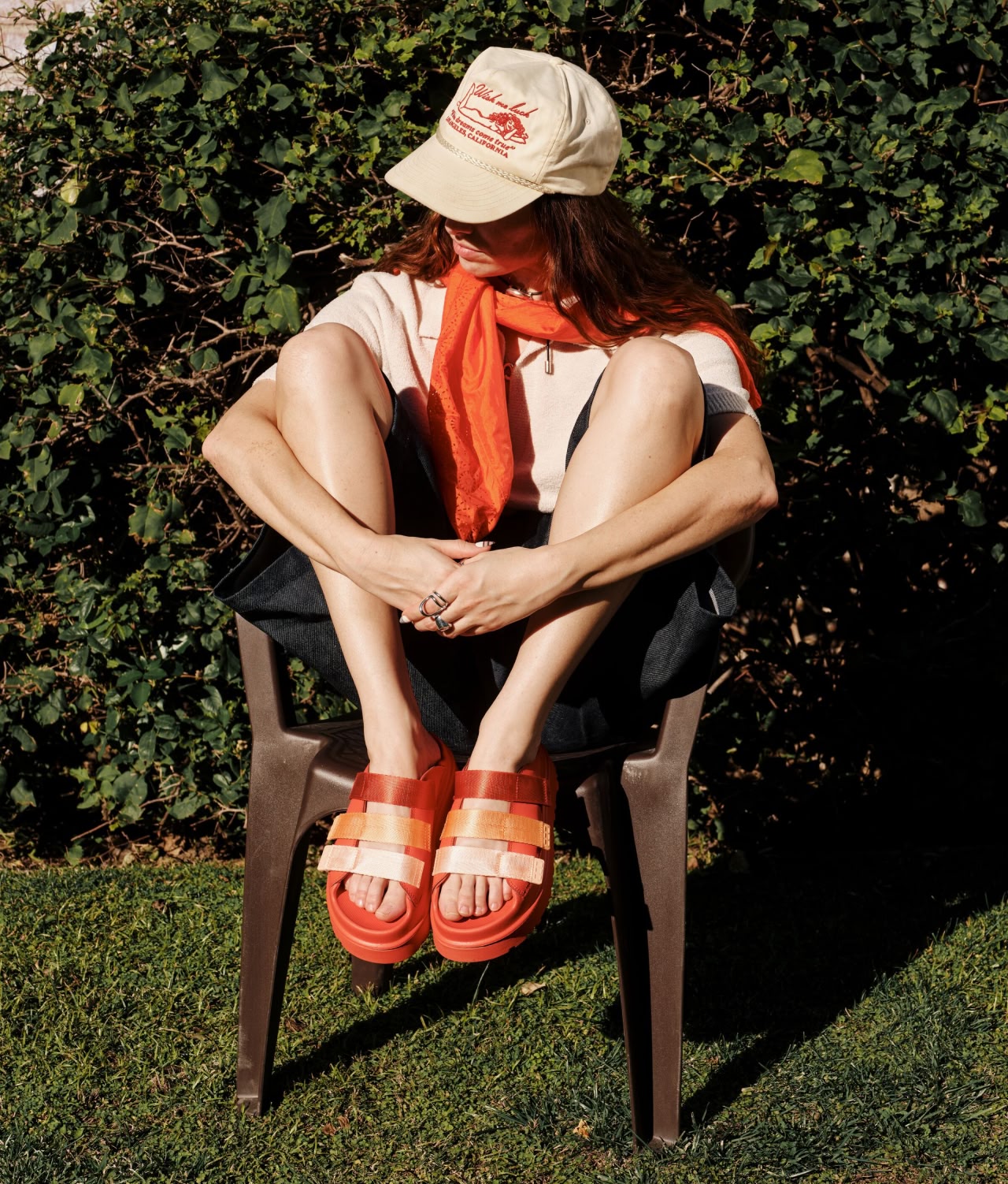 A model sat in the sun on a wooden chair, wearing the Goldenglow Slide Sandals.