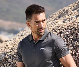 Herrenmodel trägt graues Funktions-Polo-Shirt. Natur im Hintergrund.
