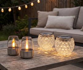 Zwei Solarkerzen, Zwei Solargläser, stehend auf Gartentisch, Terrassenambiente im Hintergrund.