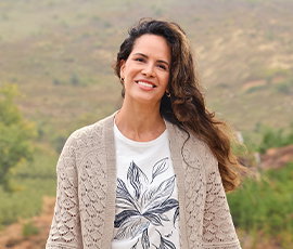 Frauenmodel trägt weißes T-Shirt mit Druck, helle, beige Strickjacke, Vorderansicht, Natur im Hintergrund.