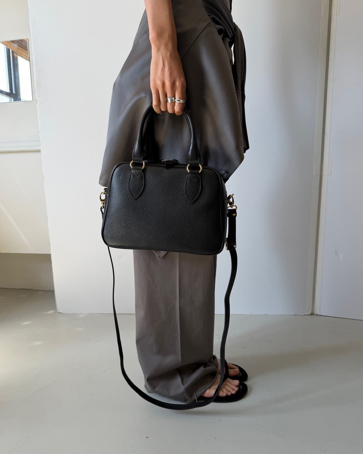 a cropped photo of a model holding the short handles of the HYER GOODS La Corsa Bowling Bag in black, with the crossbody strap hanging below the bag.